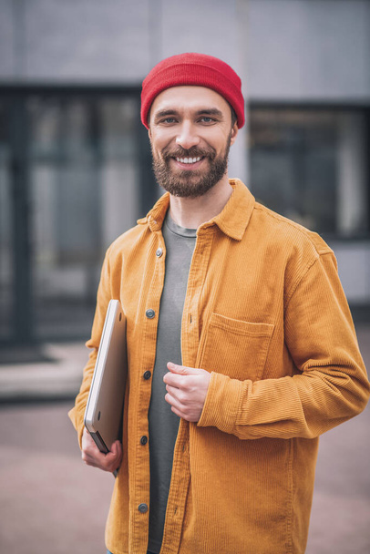 Bearded young man in a red hat with a laptop - Foto, afbeelding