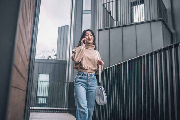 Woman in jeans and beige blouse walking and talking on the phone - Fotoğraf, Görsel