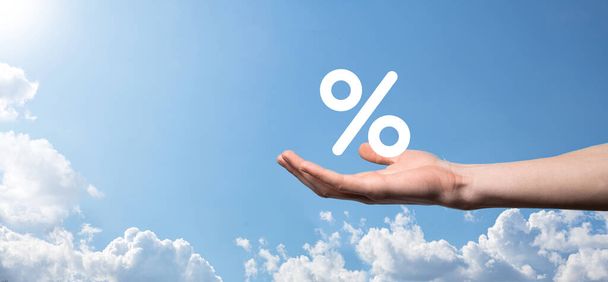 Mão masculina segurando ícone percentual de taxa de juros no fundo do céu azul. Taxa de juro financeira e taxas de hipoteca concept.Banner com espaço de cópia. - Foto, Imagem