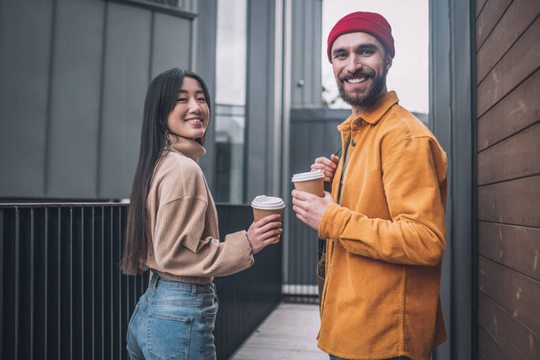 Young man and woman in casual clothes looking positive while having coffee outside - Fotoğraf, Görsel