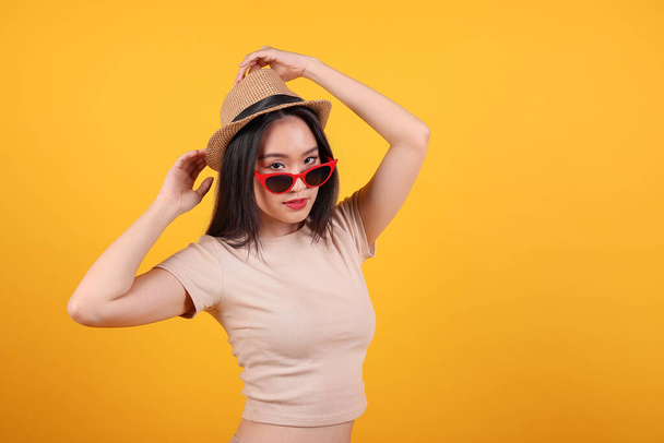 Güneydoğu Asyalı güzel kadın kırmızı çerçeveli güneş gözlüklü şapka moda zirvesi sarı turuncu arka planda mutlu. - Fotoğraf, Görsel