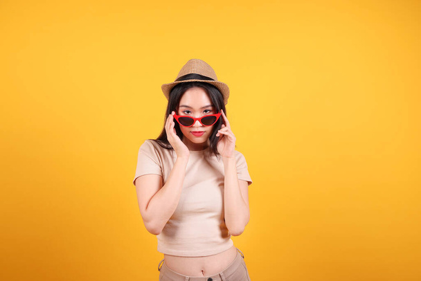 Bella giovane sud-est asiatico donna rosso telaio occhiali da sole cappello posa moda picco felice su sfondo giallo arancione - Foto, immagini