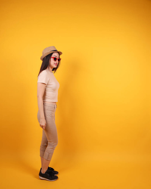 Schöne junge südostasiatische Frau rote Rahmen Sonnenbrille Hut Pose Akt Schritt nach vorne auf gelb orange Hintergrund - Foto, Bild