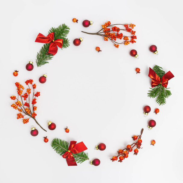 Christmas round frame from natural green fir branches and small red glitter balls and berries on white background. New Year winter holiday concept. Flat lay, top view. - Photo, image