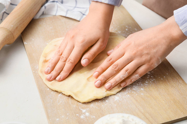 Woman kneading dough on board in kitchen, closeup - Fotó, kép