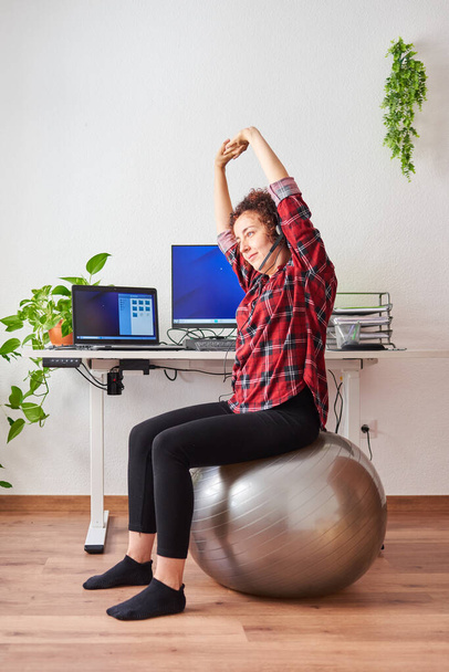Donna si allunga mentre lavora seduto su un fitball davanti alla scrivania del suo ufficio - Foto, immagini