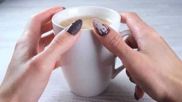 Beautiful manicured nails in the form of chocolate candies on female hands close-up and a cup of coffee. - Photo, Image