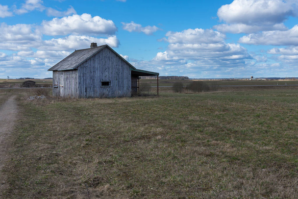 Een oud verlaten klein houten huisje in de velden wolken, naast een pad schuur of eng concept. - Foto, afbeelding