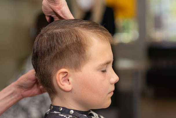 Um menino bonito recebendo corte de cabelo por cabeleireiro na barbearia. Vista lateral.Close-up. - Foto, Imagem