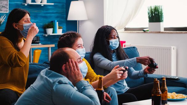 Vrienden met maskers houden controllers spelen video game - Foto, afbeelding