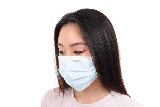Hermosa joven mujer del sudeste asiático vistiendo azul de tres capas antivirus máscara facial quirúrgica sobre fondo blanco mirar hacia abajo - Foto, imagen