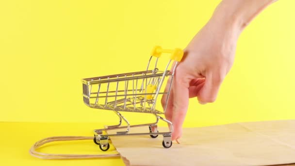 Kadın eli, sarı arka planda oyuncak bir alışveriş arabasını itiyor. Kara Cuma Alışveriş ve İndirim Konsepti - Video, Çekim