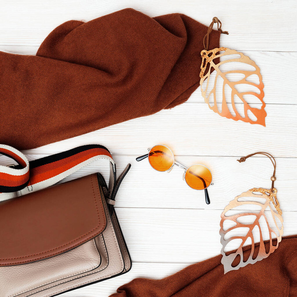 Fashion woman bag and scarf, cozy autumn female clothing decorated autumn leaves. Flat lay with comfort clothes and copy space on white wood desk. - Foto, Bild
