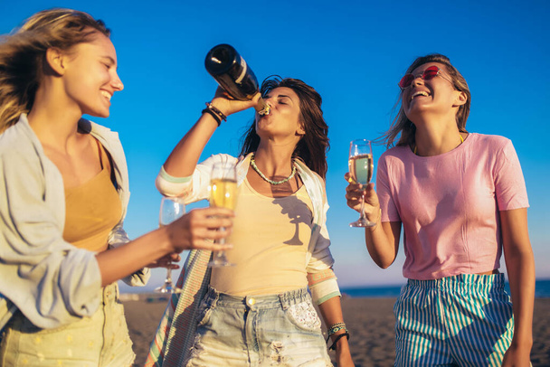 Ευτυχισμένες νεαρές γυναίκες που πίνουν σαμπάνια στο μπάτσελορ πάρτι στην παραλία. - Φωτογραφία, εικόνα