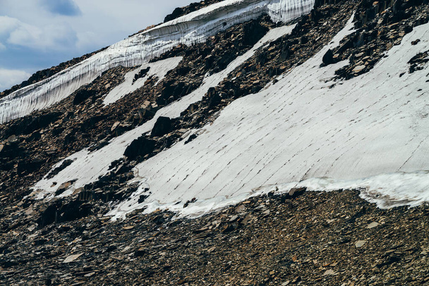 Herrlicher Blick auf einen kleinen Gletscher auf einem steinigen Hügel unter blauem Himmel mit Wolken. Schöne alpine Landschaft mit Eisgesims auf Fels. Farbenfrohe Berglandschaft in großer Höhe. Majestätische Hochlandnatur. - Foto, Bild