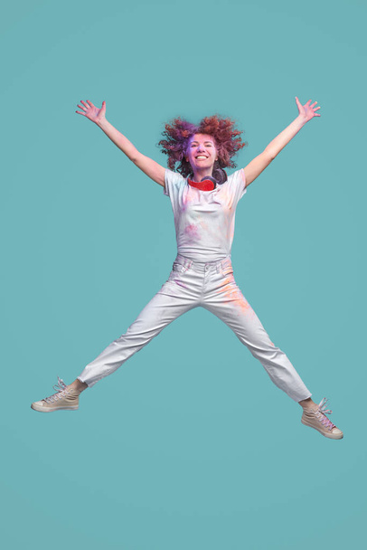 Energetic woman with Holi paints jumping in studio - Foto, imagen