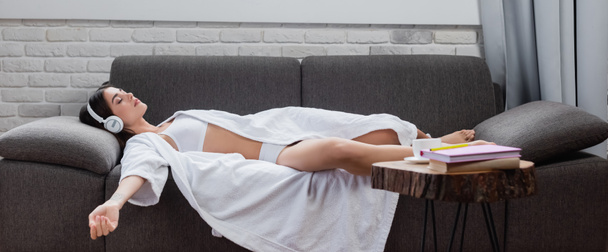 mladá dospělá žena spí ve sluchátkách na gauči doma, banner - Fotografie, Obrázek