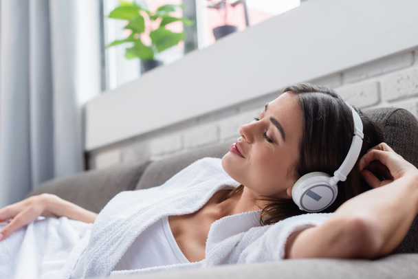 peaceful young adult woman with closed eyes resting in headphones on couch at home - Fotografie, Obrázek