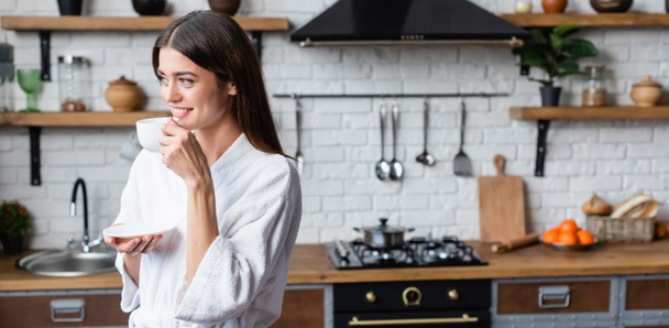 smiling young adult woman in bathrobe drinking coffee in modern loft, banner - Photo, Image
