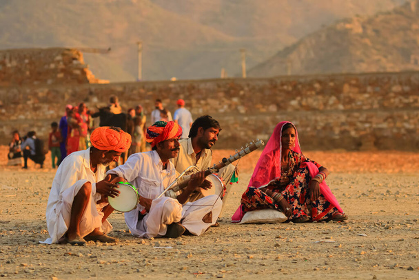 Un groupe de personnes assises sur le terrain et jouant des instruments de musique indiens traditionnels à Pushkar, Rajasthan, Inde, le 19 novembre 2018 - Photo, image