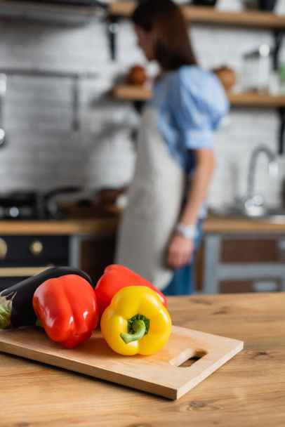 close-up zicht op verse hele paprika 's en aubergine op snijplank in de keuken - Foto, afbeelding