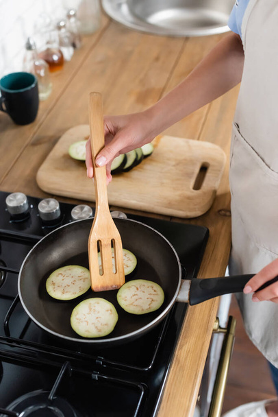 cropped view of young adult woman cooking slices of eggplant in frying pan in kitchen - Photo, Image