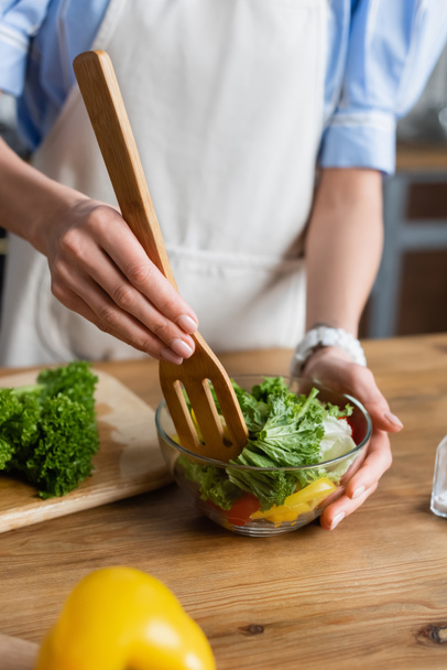 vue partielle de la jeune femme adulte mélangeant salade de légumes frais avec spatule dans la cuisine - Photo, image