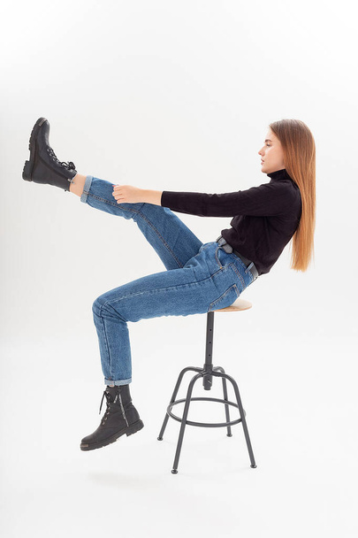 young attractive caucasian woman in black turtleneck, blue jeans pulls boots on - Zdjęcie, obraz