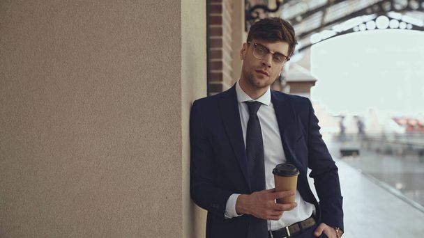 Geschäftsmann in Brille und Anzug hält Coffee to go in der Hand und posiert in Einkaufszentrum  - Foto, Bild