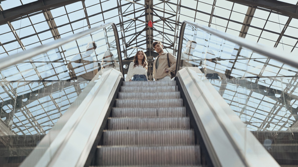 vista de ángulo bajo de la pareja cerca de escaleras mecánicas en el centro comercial  - Foto, imagen
