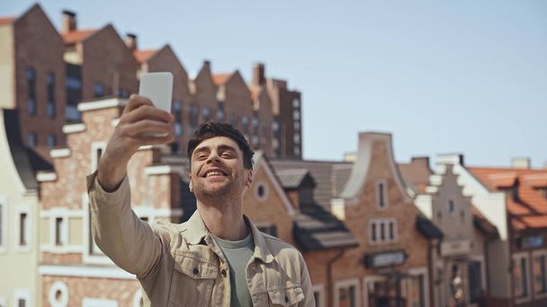 cheerful man taking selfie with blurred buildings on background  - Photo, image