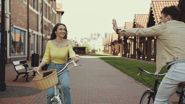 szczęśliwy mężczyzna macha ręką w pobliżu kobieta jazda na rowerze na ulicy  - Zdjęcie, obraz