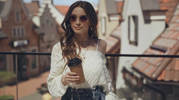 スタイリッシュな若い女性がコーヒーを持って外に出て  - 写真・画像