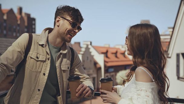 stylish couple smiling while holding paper cups outside  - Фото, изображение