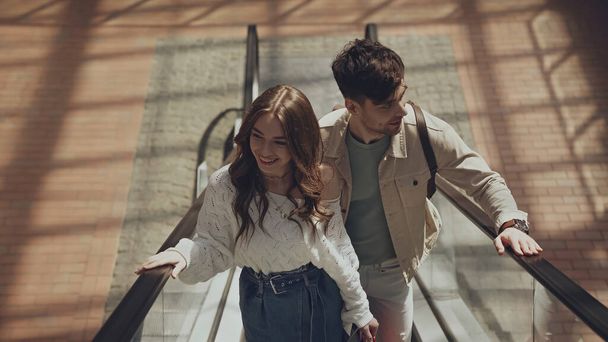 high angle view of happy man and woman on escalator in shopping mall - Photo, image