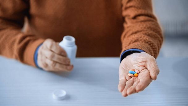 primer plano vista de frasco de la medicina y píldoras multicolores en manos de un hombre de edad avanzada sobre fondo gris - Foto, Imagen