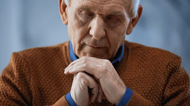 portrait of elderly man with closed eyes and clenched hands near face on grey background - Photo, Image