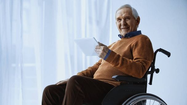 cheerful pensioner in wheelchair holding tablet in hand at retirement home - Photo, Image