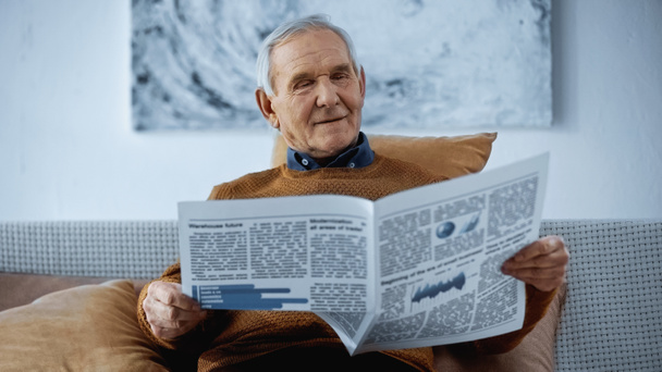 старший чоловік сидить на дивані і читає газету вдома
 - Фото, зображення