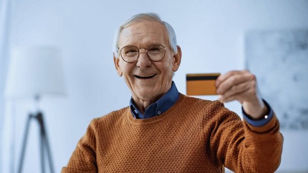 現代のリビングルームでクレジットカードを持っているメガネの高齢者の笑顔 - 写真・画像