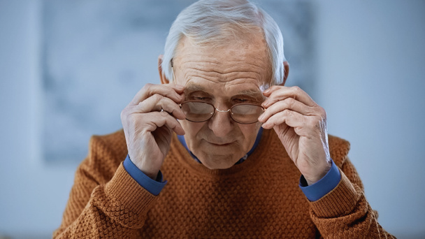 concentrated elderly man adjusting glasses on grey background - Photo, Image