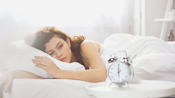 awake young woman looking at retro alarm clock  - Foto, afbeelding