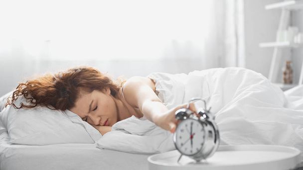 displeased young woman reaching retro alarm clock in morning  - Foto, Bild