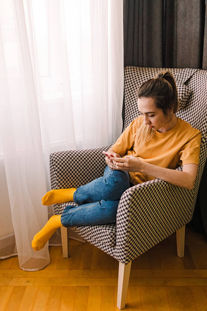 Young woman focused on her smartphone sitting in the armchair - Photo, image