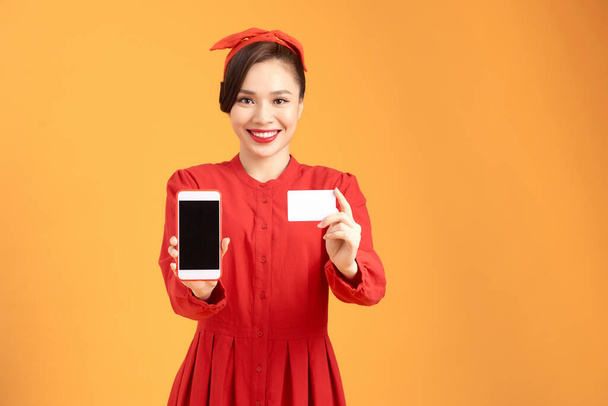Fénykép érzelmi izgatott csinos fiatal nő elszigetelt sárga háttér segítségével mobiltelefon gazdaság hitelkártya. - Fotó, kép