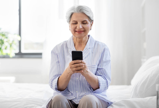 happy senior woman with smartphone on bed at home - Фото, зображення