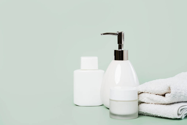 Skincare products.Cream банка, лосьон, жидкое мыло диспенсер и полотенце с копировальным местом на зеленом фоне - Фото, изображение