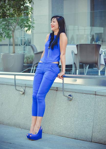 Una mujer de traje azul y pelo largo oscuro espera a sus amigos en la ciudad. El estilo de vida de una gran metrópolis y ciudadanos - Foto, Imagen