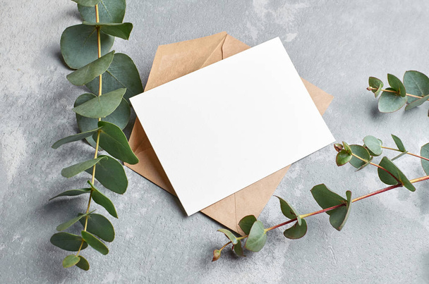 Invitation or greeting card with envelope and fresh eucalyptus twigs on grey concrete background, copy space - Foto, Imagem
