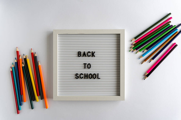 Üzerinde "Okula Dönüş" ü heceleyen kelimeler olan beyaz arka planda, beyaz arka planda, yatay ve renkli kalemler olan bir pano. - Fotoğraf, Görsel